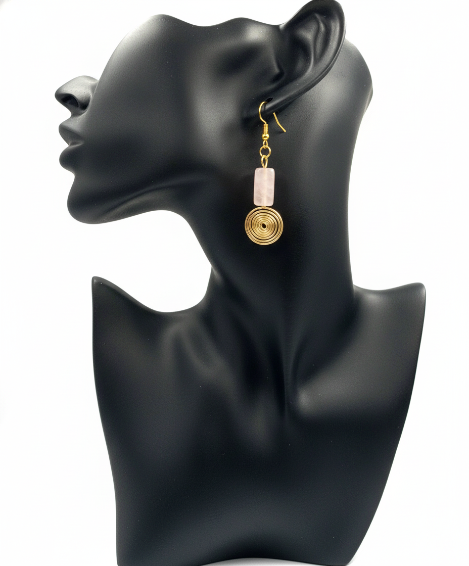 A pair of gold-colored dangle earrings with a swirl design displayed on a black mannequin ear.