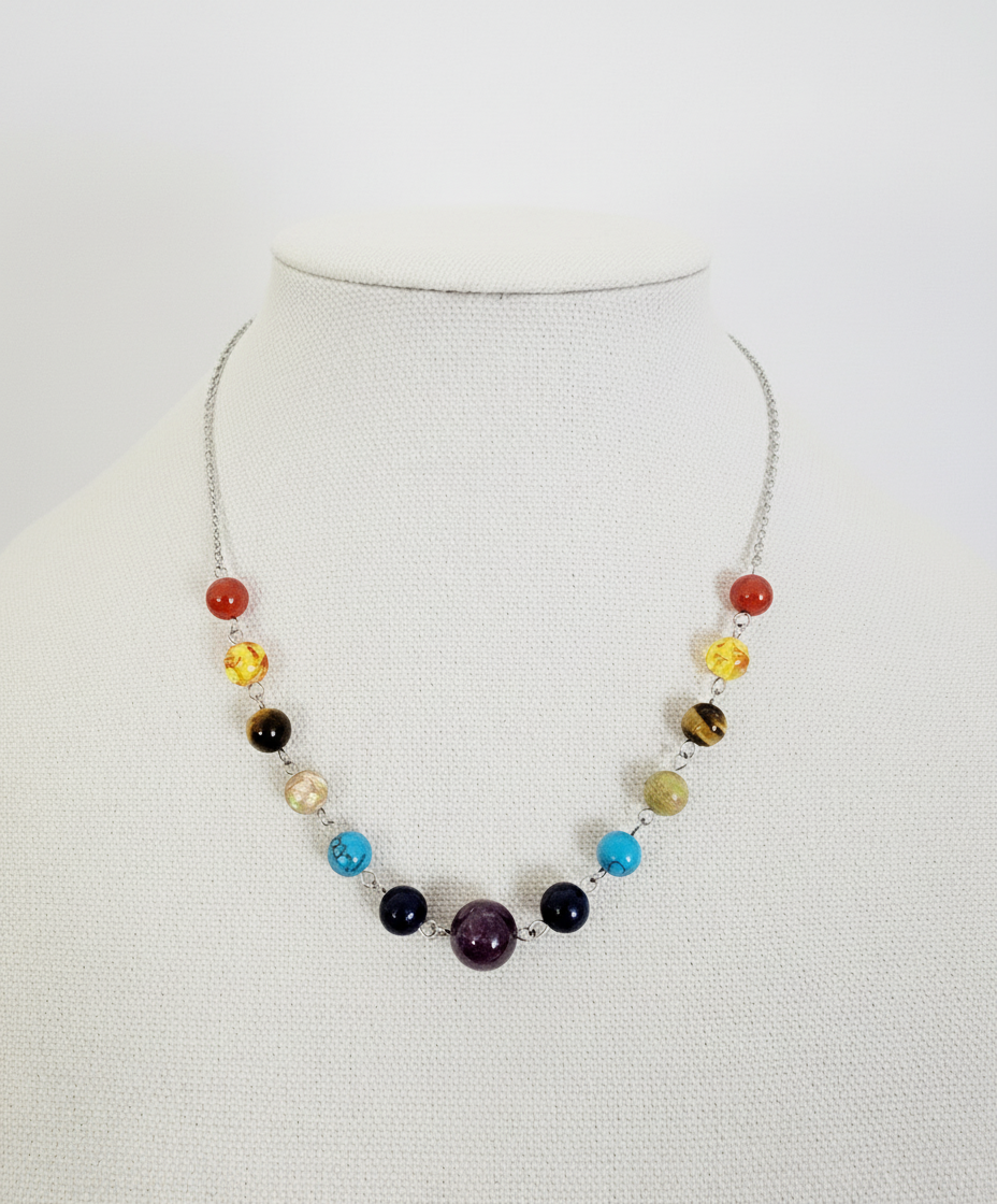 A beaded chakra necklace displayed on a mannequin torso, featuring a series of multicolored beads on a silver chain.