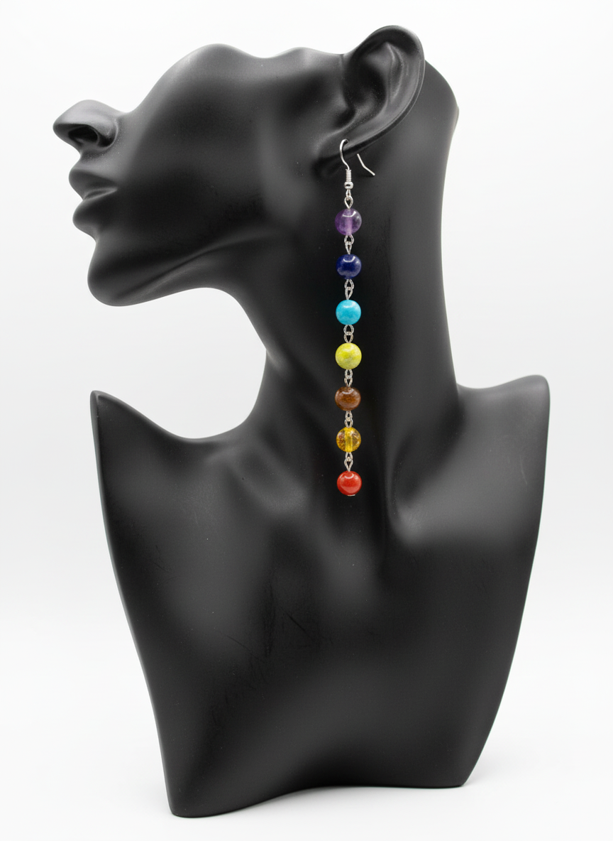 A pair of chakra dangle earrings with colorful beads in order from top to bottom representing the seven chakras, displayed on a black mannequin ear.