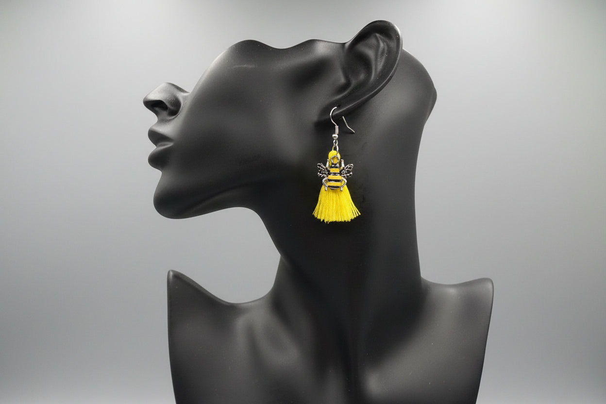 Yellow tassel earrings adorned with a bee charm on a black mannequin head against a gray background