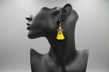 Yellow tassel earrings adorned with a bee charm on a black mannequin head against a gray background