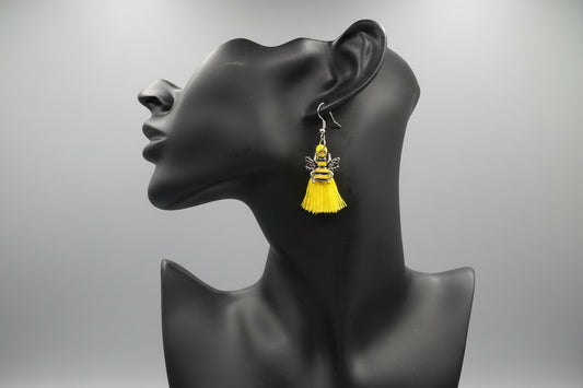 Yellow tassel earrings adorned with a bee charm on a black mannequin head against a gray background