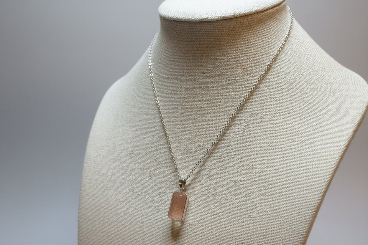 Necklace with a cherry quartz pendant on a mannequin bust against a neutral background