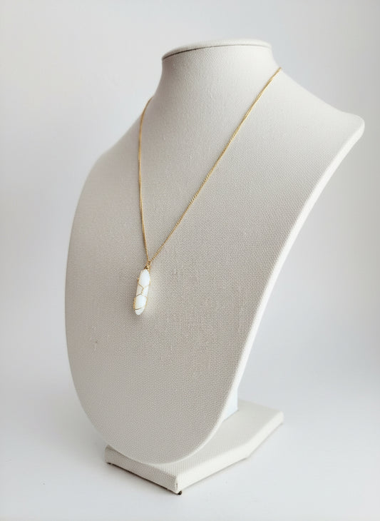 Necklace with a large white gemstone pendant on a linen mannequin bust against a white background